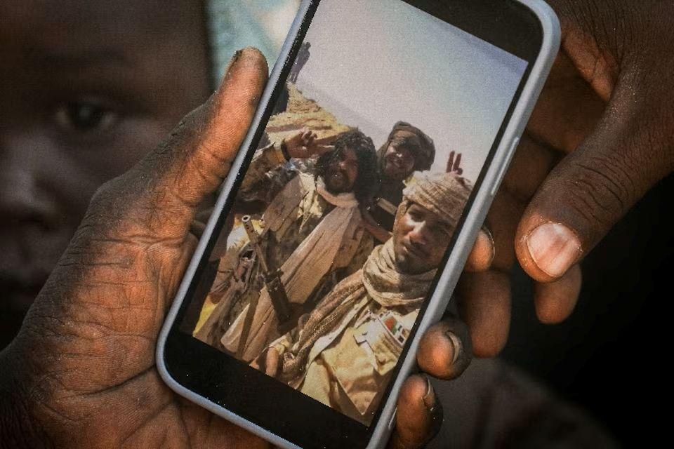 لاجئة سودانية من الفاشر تمسك هاتفاً يعرض مقطعاً مصوراً للفاتح عبد الله إدريس، المعروف باسم "أبو لولو"، في شرق تشاد في 23 نوفمبر/تشرين الثاني 2025.